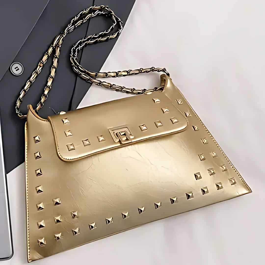 Gold studded leather handbag with chain strap on a white and grey surface