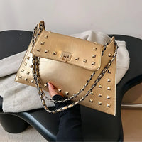Gold studded leather handbag with chain strap on a black chair