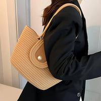 Woman in black blazer carrying a beige woven straw shoulder bag indoors