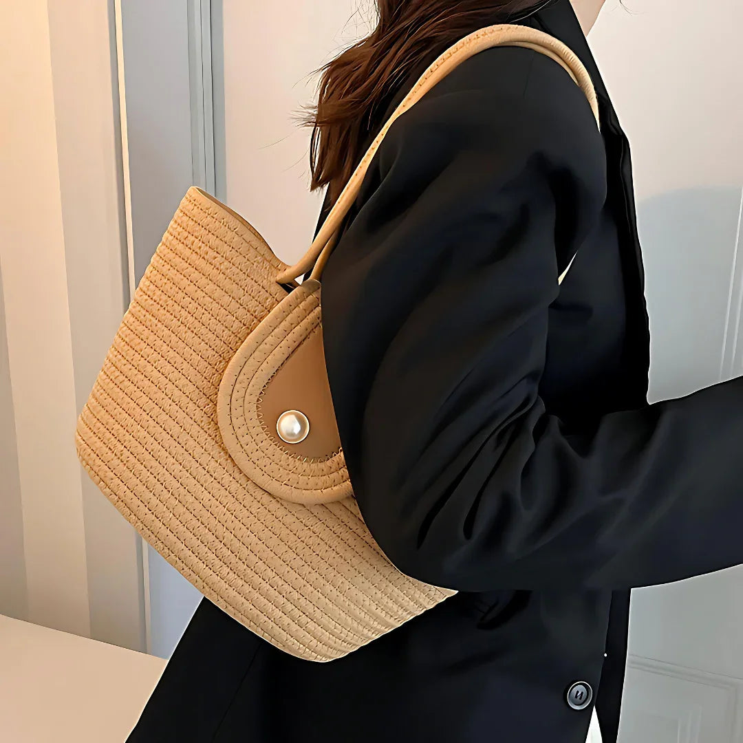 Woman in black blazer carrying a beige woven straw shoulder bag indoors