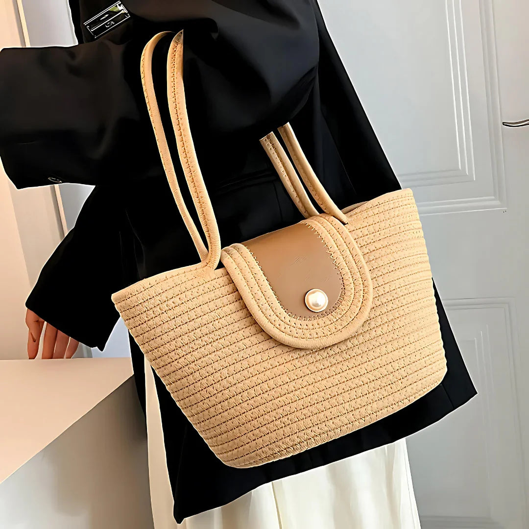 Woman wearing black coat holding beige woven tote bag with leather flap and pearl button