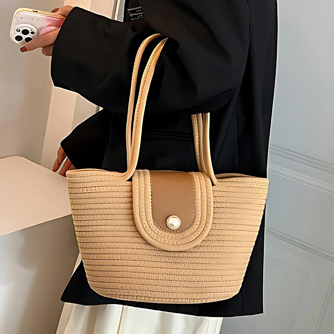Woman holding beige woven handbag with double straps and button flap, stylish outfit