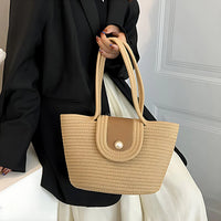 Woman in black blazer holding beige woven tote bag with double handles and button flap