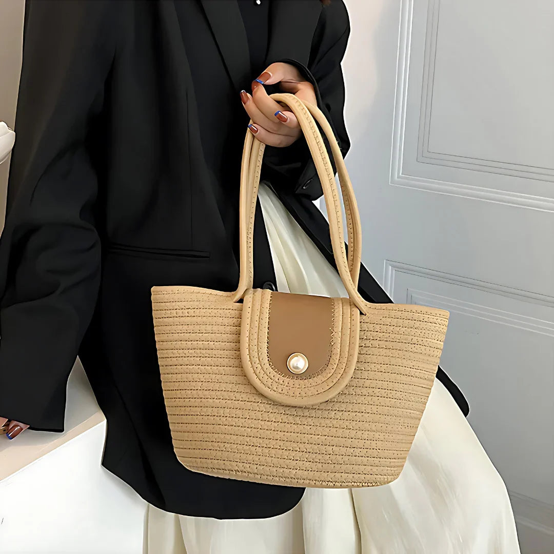 Woman in black blazer holding beige woven tote bag with double handles and button flap