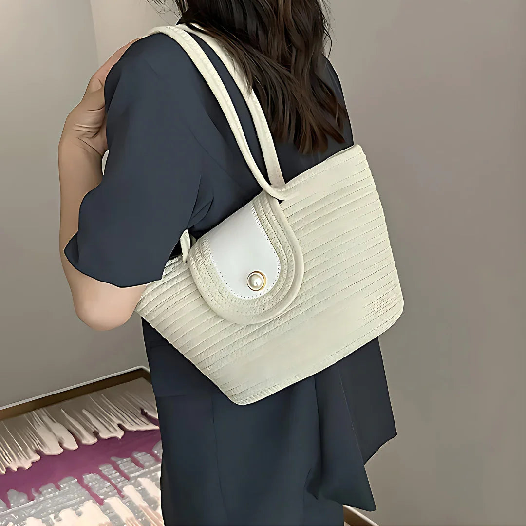 Woman in black dress carrying a cream quilted shoulder bag with gold button accent