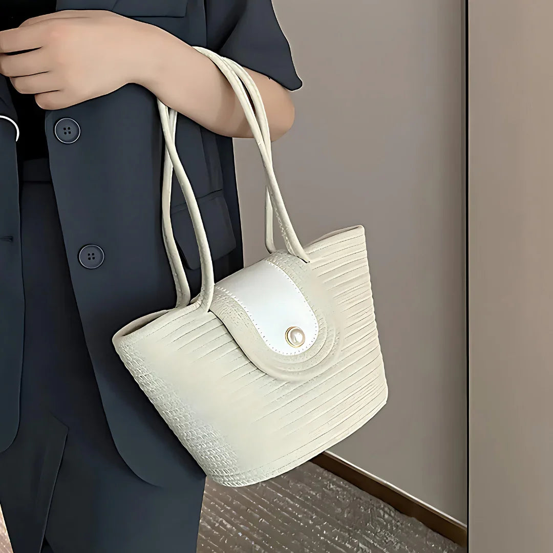 Woman holding cream woven tote handbag with button closure, wearing navy blazer
