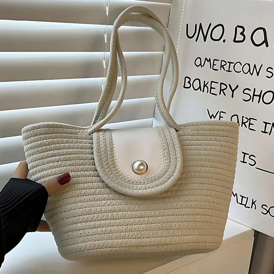 Beige woven straw tote bag with white flap and button, held near window blinds