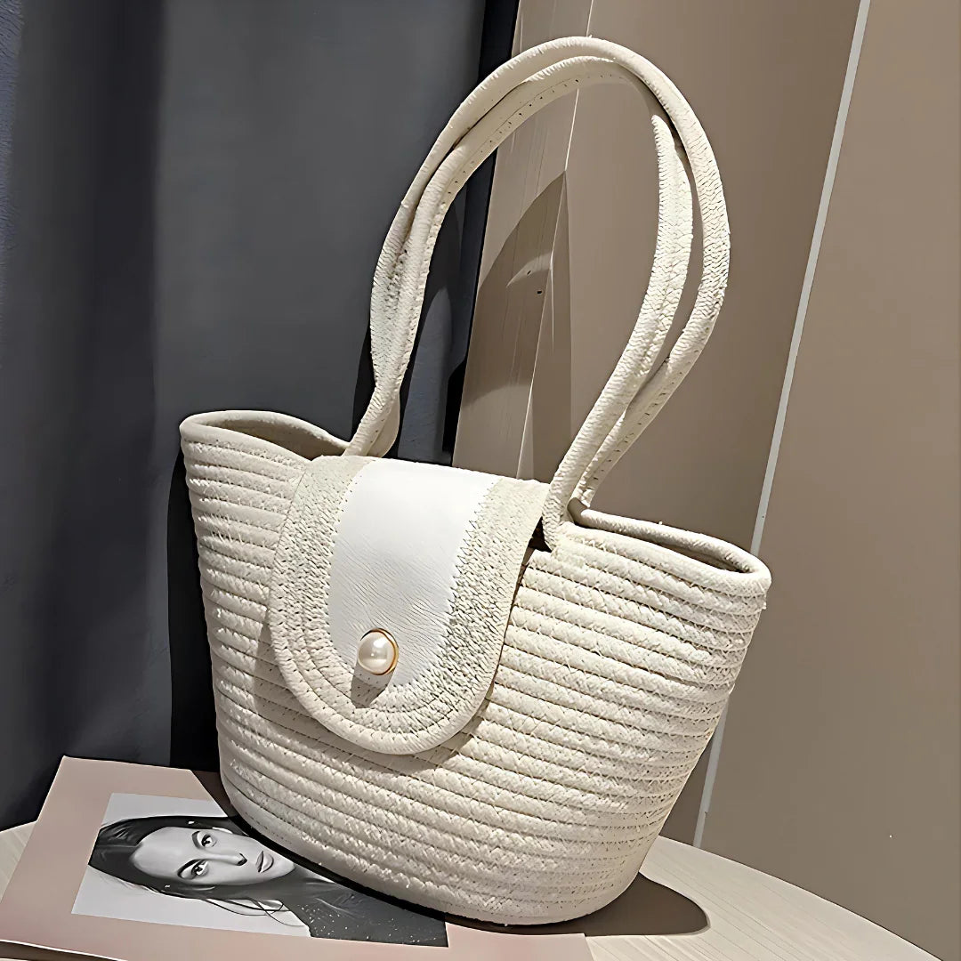 Elegant white woven tote bag with pearl button on flap, resting on a table indoors