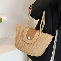 Woman wearing black blazer holding beige woven tote bag with button-flap closure