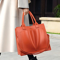 Woman holding large orange leather tote bag outdoors, wearing a light coat