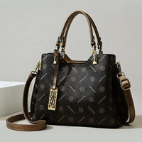Elegant black and brown leather handbag with floral pattern and gold hardware on neutral background.