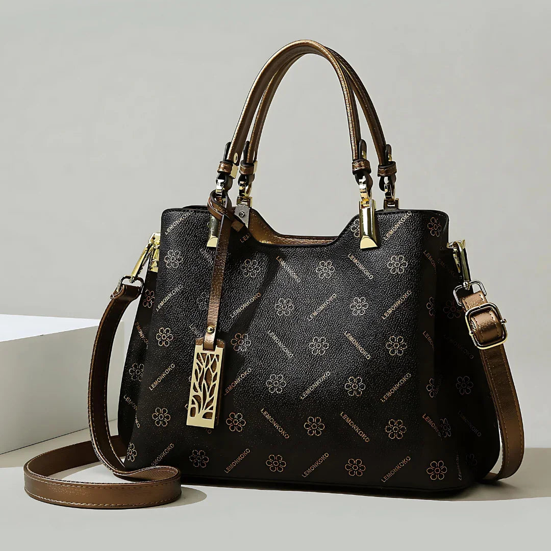 Elegant black and brown leather handbag with floral pattern and gold hardware on neutral background.