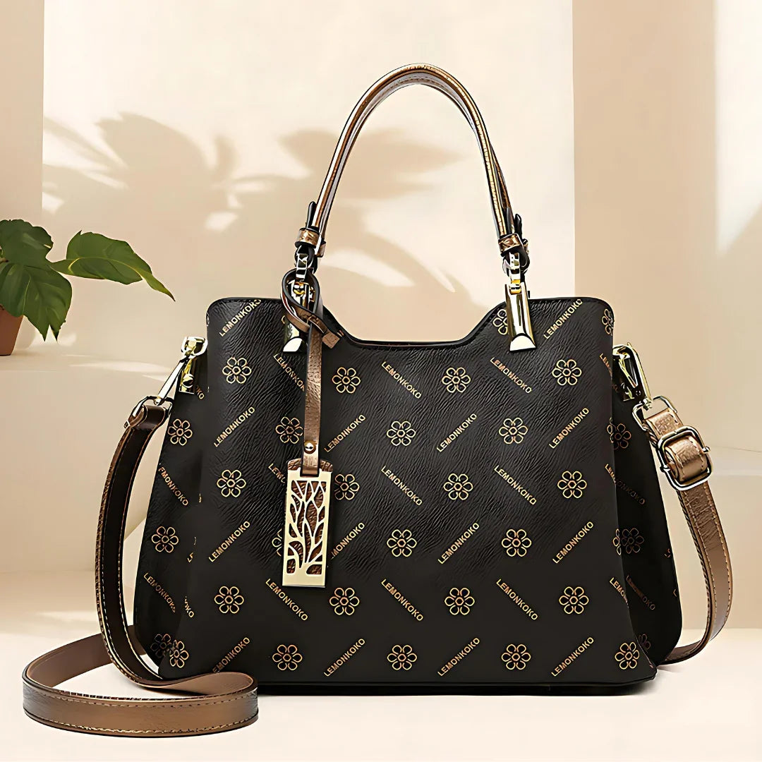 Black LEINWONKO handbag with gold floral pattern and leather straps on a beige background