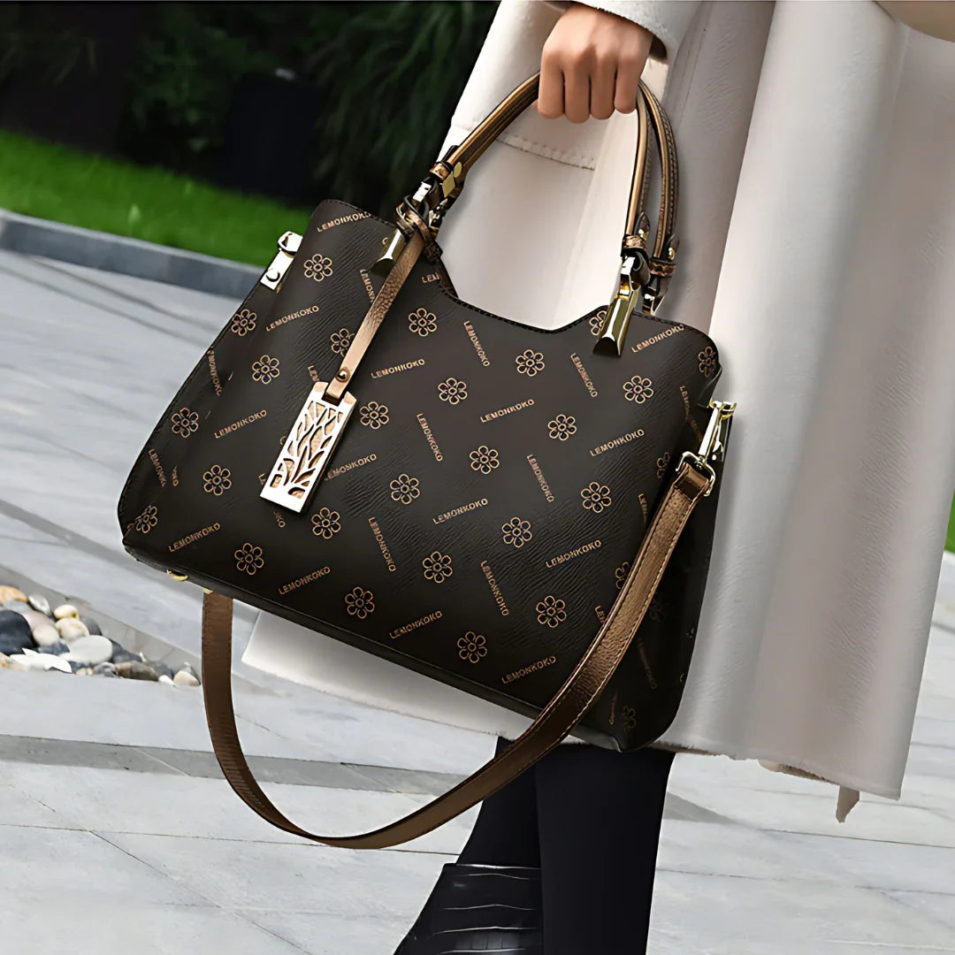 Woman holding brown designer handbag with floral print and gold hardware outdoors