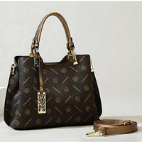 Brown designer handbag with floral pattern, gold hardware, and detachable strap on table