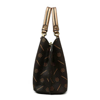 Side view of a black designer handbag with gold floral pattern and dual handles