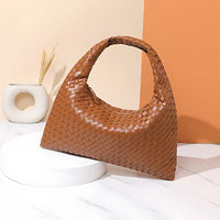 Brown woven leather hobo handbag on white marble with modern vase and orange backdrop
