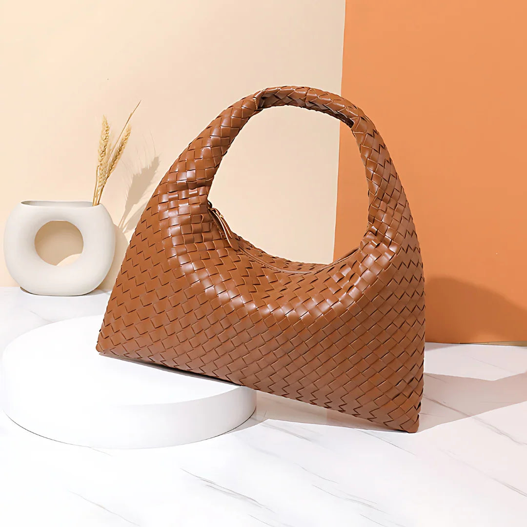 Brown woven leather hobo handbag on white marble with modern vase and orange backdrop