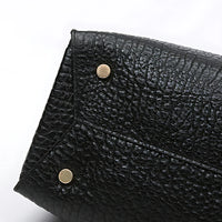 Textured black leather handbag corner with gold metal feet on white background