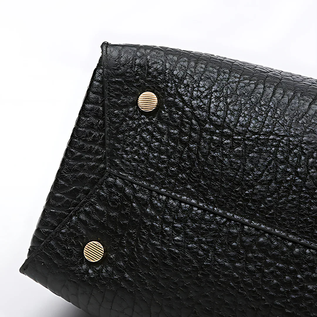 Textured black leather handbag corner with gold metal feet on white background