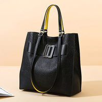 Black textured tote bag with yellow-lined handles and large buckle detail on beige background