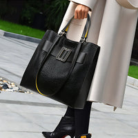 Woman carrying large black leather tote bag with textured design and buckle detail outdoors