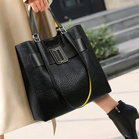 Woman carrying large black textured leather tote bag with buckle detail on city sidewalk