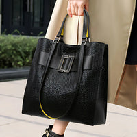 Woman holding large black textured leather tote bag with buckle detail outdoors