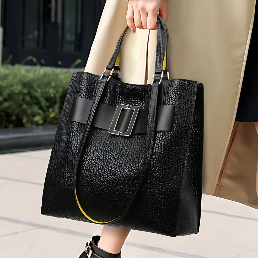 Woman holding large black textured leather tote bag with buckle detail outdoors