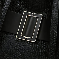 Close-up of black leather bag with rectangular gold buckle and textured finish