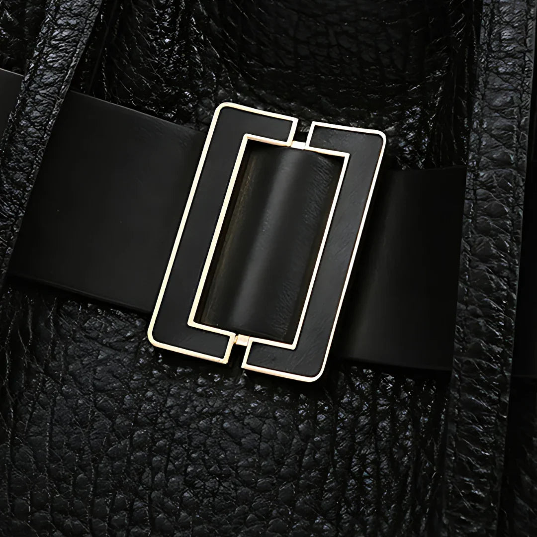 Close-up of black leather bag with rectangular gold buckle and textured finish