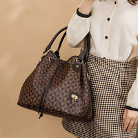Woman holding geometric brown leather tote bag, houndstooth skirt, cream blouse