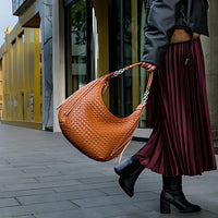 Woman with large woven brown leather hobo bag, pleated skirt, and black boots on city street
