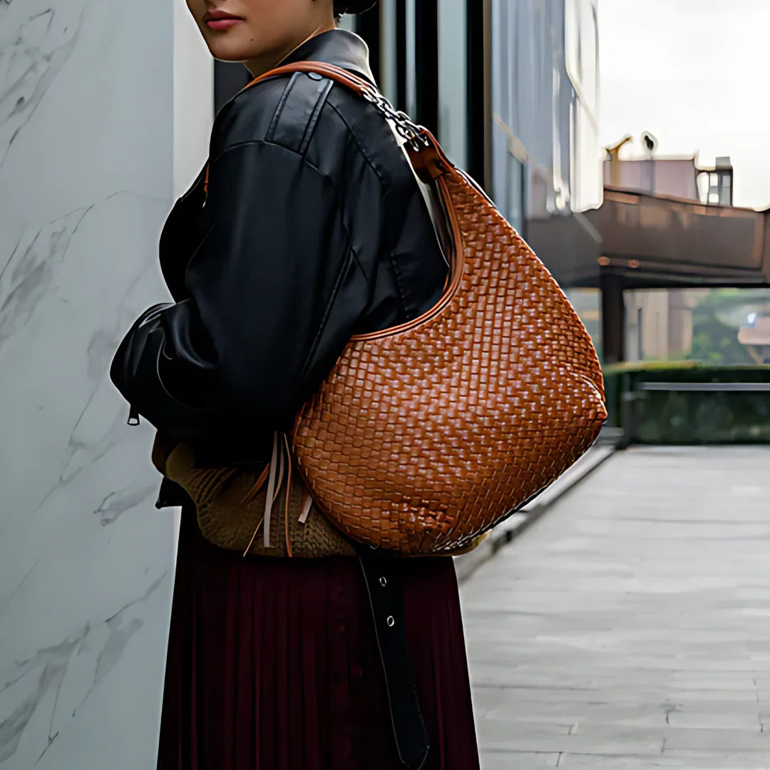 Woman outdoors with brown woven leather shoulder bag, black jacket, modern city background