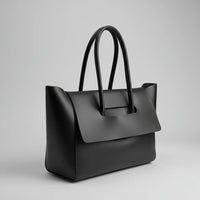 Minimalist black leather tote bag with double handles on a plain gray background.