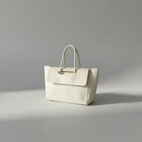 Minimalist cream leather tote bag with top handles on a light gray background