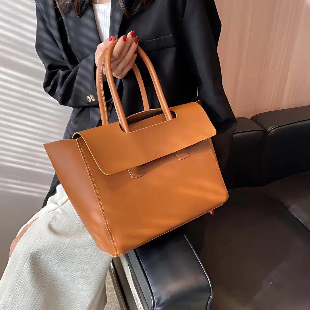 Woman holding brown leather tote bag in modern office setting