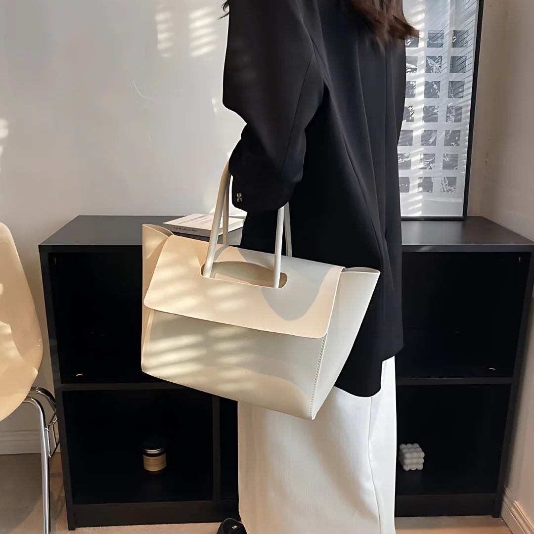 Woman in black blazer holding large white leather tote bag in modern office setting