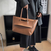 Woman in black outfit holding a large brown leather tote bag indoors