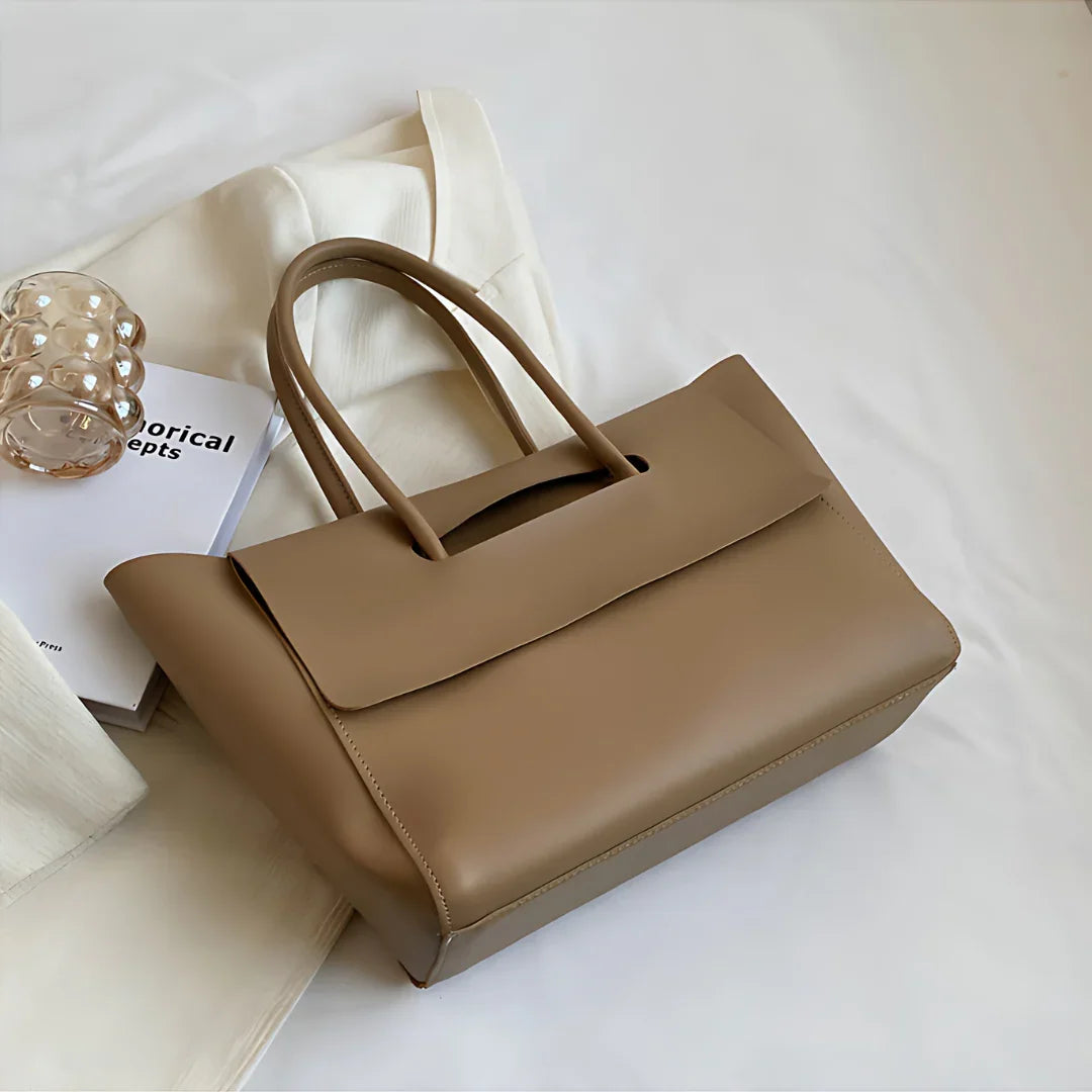 Taupe leather tote bag on white fabric with clear bracelet and book for minimalist style