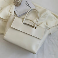Minimalist white leather tote bag on cream blazer with book and decorative glass