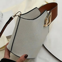 Textured white leather handbag with brown strap and gold buckle, modern minimalist design