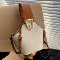 Chic bucket bag with white pebbled leather, brown strap, and gold buckle detail on chair