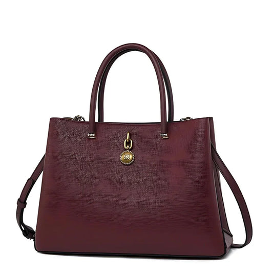 Elegant burgundy leather handbag with gold charm and dual top handles on white background