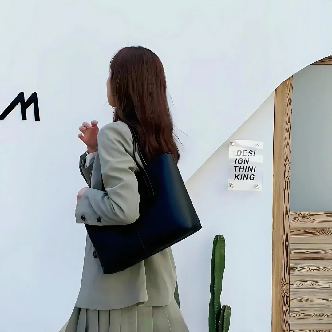 Woman in gray blazer with black tote bag stands by white wall, modern office design