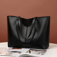 Black leather tote bag on white table with open magazine, brown background
