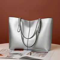 Silver leather tote bag with double handles on a table beside an open magazine
