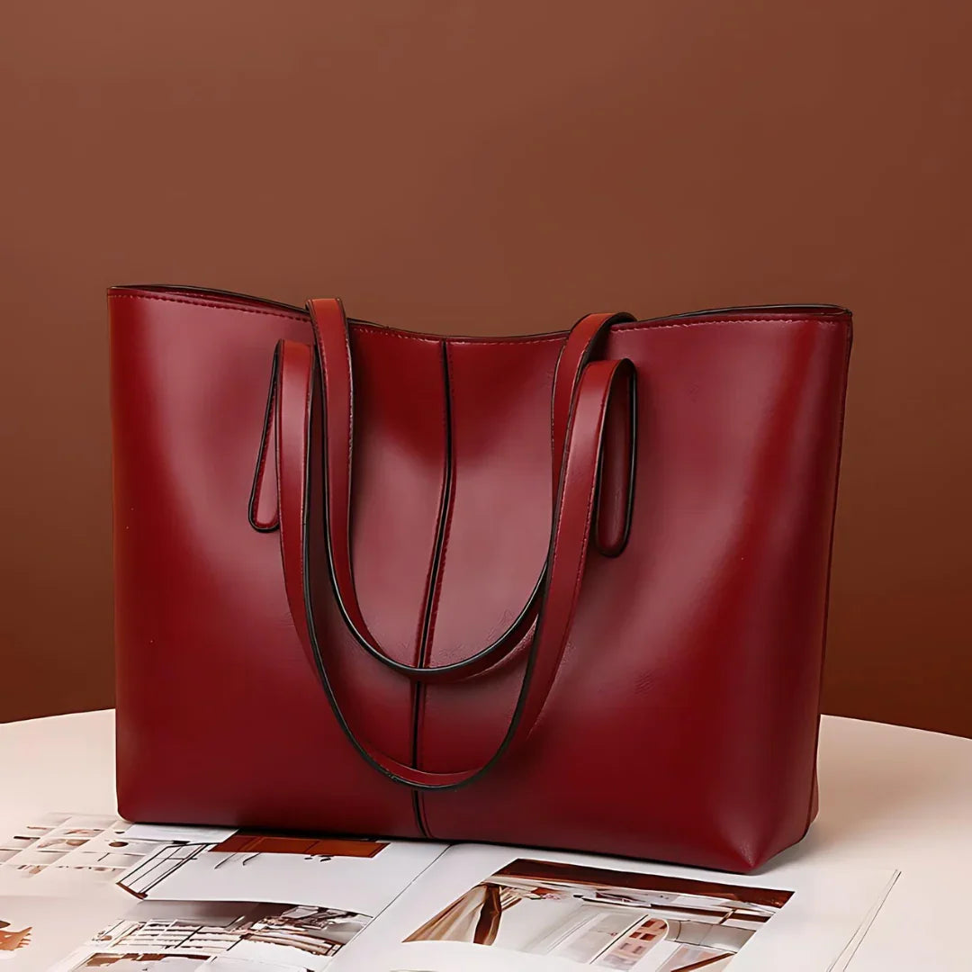 Large red leather tote bag with double handles on a white table, brown background