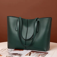 Dark green leather tote bag with double handles on a table with magazines, brown background