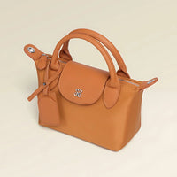Tan leather handbag with top handles, silver logo, and luggage tag on beige background